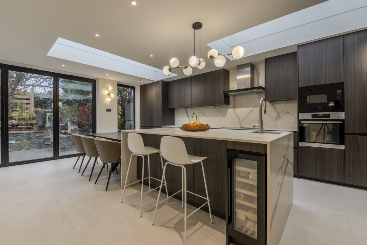 Luxury modern kitchen with dark wood cabinetry, large island, skylight and open-plan layout in West London home