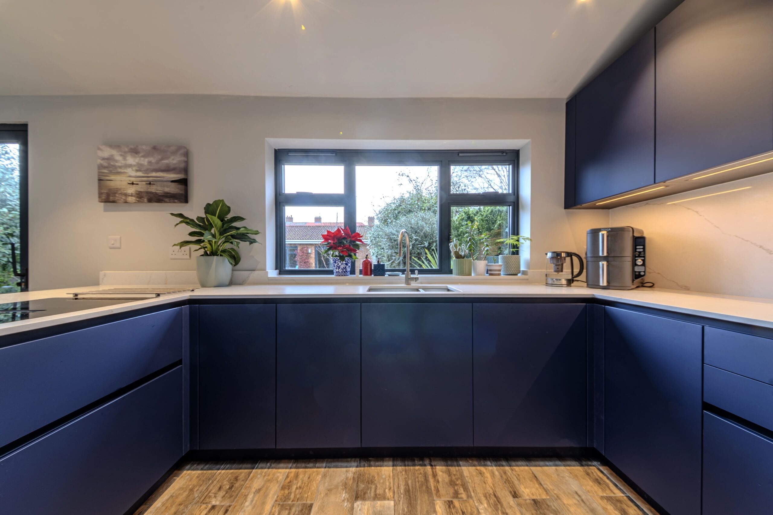 Contemporary navy blue U-shaped kitchen with handleless cabinets, white worktops and window-led natural light